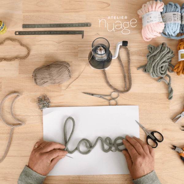 mains réalisant un tricotin "love", table vue de haut, avec des outils